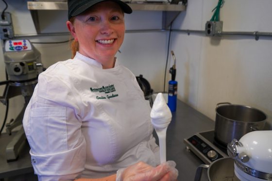 person in a black hat in a white shirt holding a spoon covered in whipped cream